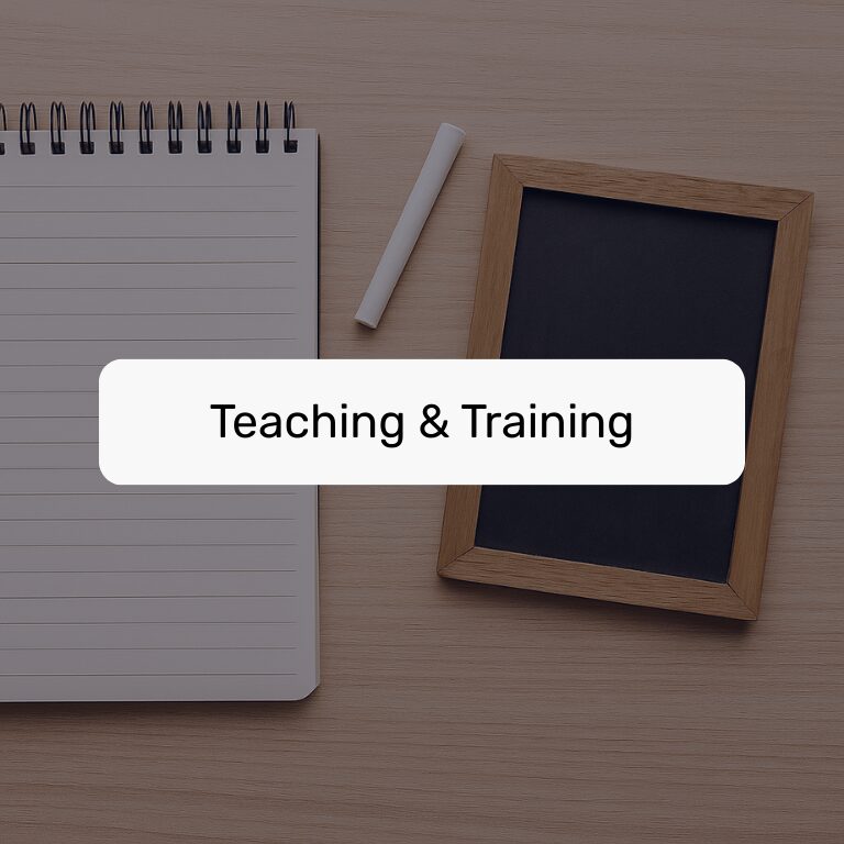 Flat lay of notebook, chalk, and chalkboard on a desk, labeled "Teaching & Training."